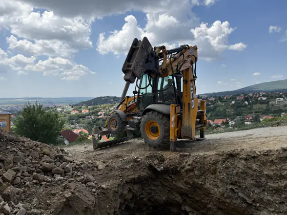 Kotró-rakodó a dombtetőn, gomolyfelhők alatt
